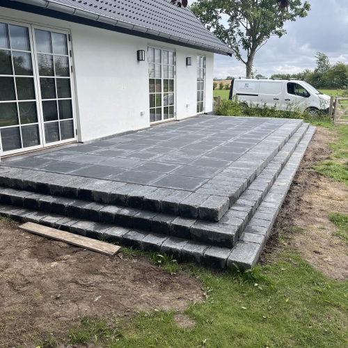 Opbygning af en ny terrasse i fliser med trappe effekt ved et hvidt hus i Korsør