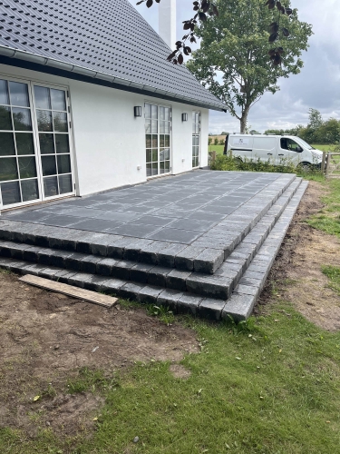Opbygning af en ny terrasse i fliser med trappe effekt ved et hvidt hus i Korsør 